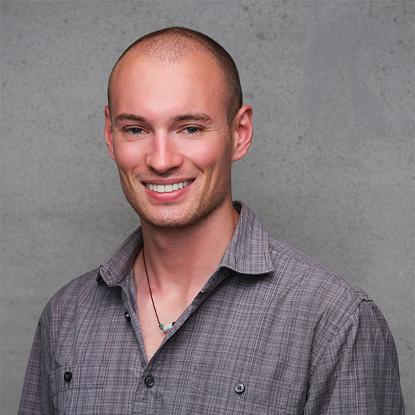 person with shaved head sitting infront of a grey background