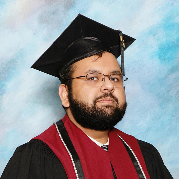 Graduation photo of person wearing cap and gown in front of light blue background.