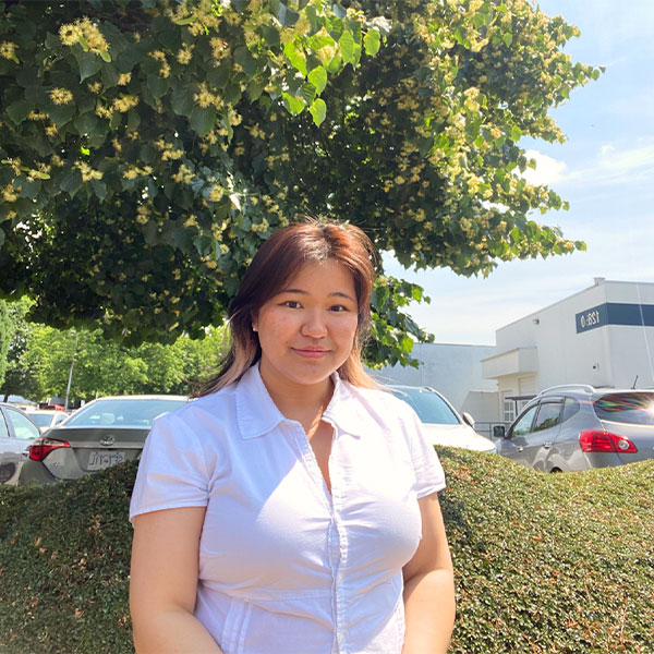 person standing outside in front of a tree and bush.